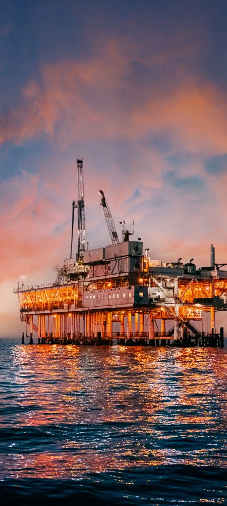 A stunning sunset photo showcases offshore oil drilling in Huntington Beach, California, with vivid hues casting a glow on industrial equipment